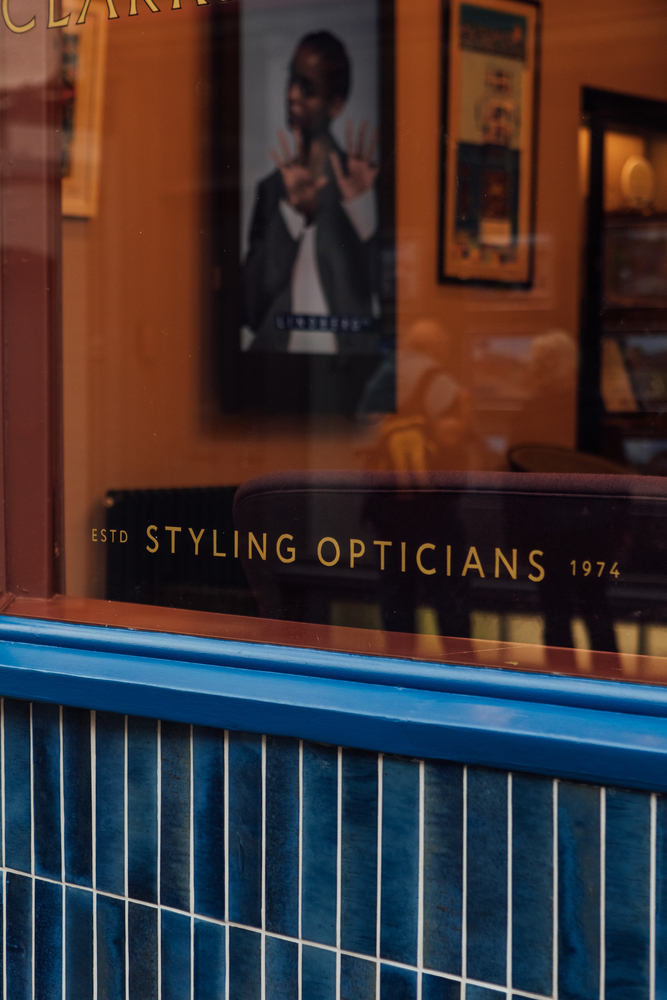 Clarke & Roskrow - Styling Opticians Estd 1974 - signwriting on shop front window with blue tiles below. 